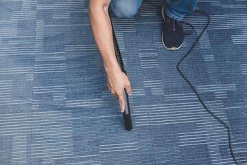 A man cleans the carpet flooring of an office with an upright vacuum cleaner with an attached extension wand. © Mdv Edwards