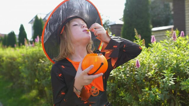 Pretty girl in halloween witch costume eating gummy worm in village outdoors, trick or treat concept. 