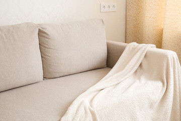 Soft fluffy warm blanket on light beige sofa at living room. Relaxing place at home. Closeup. Side view.