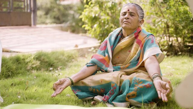 Senior woman meditating with eyes closed at morning in garden - concept of relaxation, wellbeing and self care