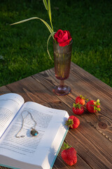 Strawberries, a book, a rose lie on a wooden table. rustic still life
