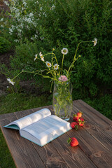 Evening still life. Strawberries, wild flowers book.