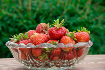 Strawberries in a crystal vase on a wooden table in the garden