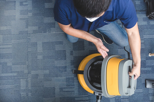 A janitor opens up the lid of a vacuum cleaner to inspect and clean out the contents. At an office room.