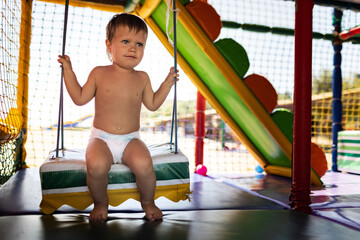 Boy riding a swing in a playroom on a summer day