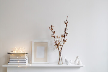 Scandinavian style room interior in white tones. A vase with cotton flowers, a stack of books, a...