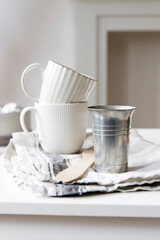 Two white mugs, a kitchen towel, a napkin and wooden frying utensils on the table. Defocus.