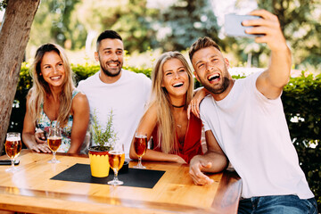 Group of young people have a good time in backyard taking selfie at table and drink beer