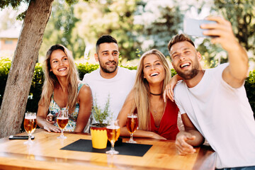 Group of young people have a good time in backyard taking selfie at table and drink beer