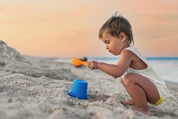 Boy playing with toys on the beach building beads and turrets smiling at someone behind the scenes on summer vacation