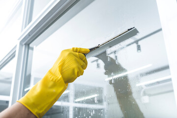 A man cleans the surface of an interior office window with a glass wiper or squeegee. The surface...