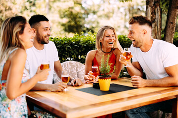 Group of young people have a good time in backyard at a wooden table they laugh and drink beer