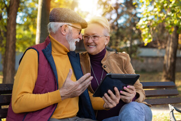 Smiling senior active couple sitting on the bench looking at tablet computer