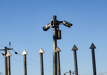 Video cameras over iron fence spikes on blue sky