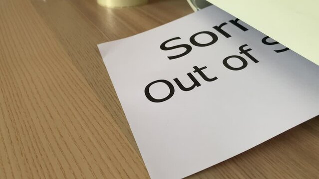 Printing &ldquo;Sorry..Out of Service&rdquo; text written message on paper sheet document. Close up A4 white page being printed from multifunction printer scanner on wooden desk in office. Hand take paper out