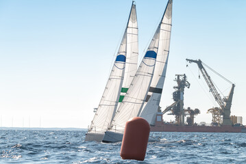 Two sport sailboats next to a turning buoy