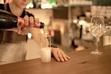a man in a light apron behind the bar pours champagne into a glass