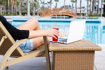 a girl lies near the pool in a cocktail and laptop