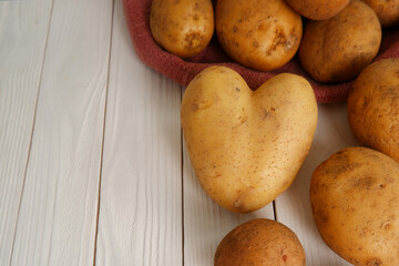 Heart-shaped potatoes poured out of a bag on a white wooden background.The concept of natural farm vegetables. Seeds of potato tubers.Copyspace