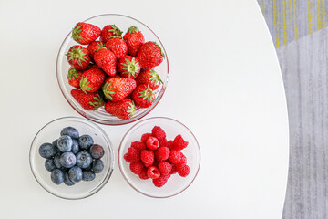 An assortment of berries, juicy strawberries, blueberries and raspberries arranged in glass bowls...
