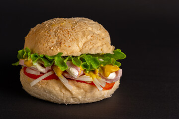 Hamburger with ham, lettuce, tomato, onion, mayonnaise and mustard on a black background.