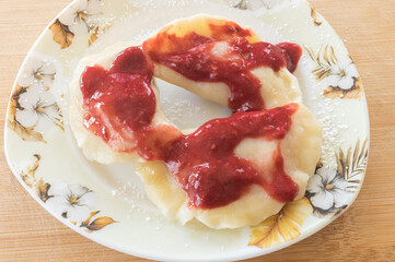 Close view on a plate with traditional Ukrainian desert - vareniky stuffed with cherry berry, flavored with sugar powder and fresh raspberry and honey mix.
