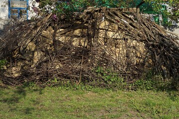 a large pile of brown bricks overgrown with gray dry branches of plants in green grass on the street