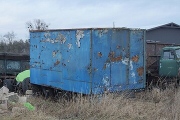 Fototapeta na wymiar one big blue old iron trailer in rust on the street overgrown with gray dry grass 