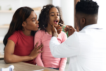 Black pediatrician checking patient little girl throat