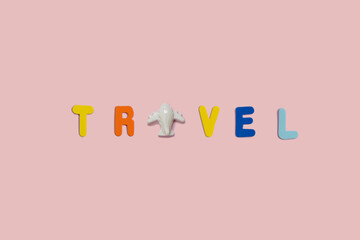 Word Travel spelled with vivid colorful foam letters on a pink background with copy space and a small toy plane. Creative vacation and visit the world cocept. Greeting summer card.