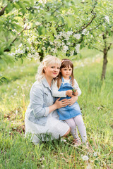 Fototapeta premium Cute blonde woman with her little daughter in a spring blooming garden