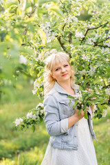 cute blonde woman near a flowering apple tree. Portrait of a girl in a spring garden