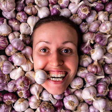 The girl holds a garlic bulb in her teeth. Portrait of a woman among many garlic bulbs