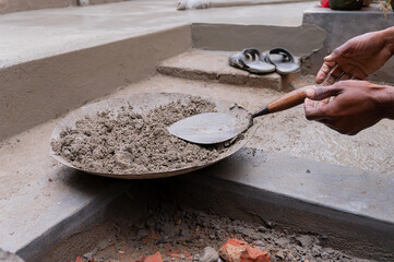 Indian labour preparing cement for plastering manually on bucket using trowel with bare hands....