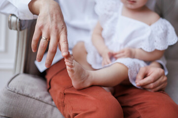 Fototapeta na wymiar Closeup of little baby girl's feet in hands of her father. Fingers of man playing with girl's feet. Hands holding small daughter's legs, tenderly and accurately