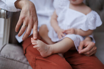 Closeup of little baby girl's feet in hands of her father. Fingers of man playing with girl's feet. Hands holding small daughter's legs, tenderly and accurately