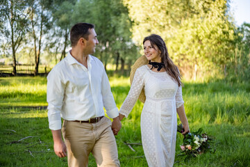 Obraz premium Just married loving hipster couple in wedding dress and suit on a green field in the woods. happy bride and groom walking running and dancing on a summer meadow. Romantic married to a young family