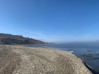 pebbly bank of the Volga river in April in Fog and with blue sky