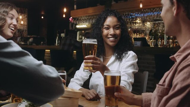 Multi-ethnic group of friends clinking glasses of beer at a restaurant.