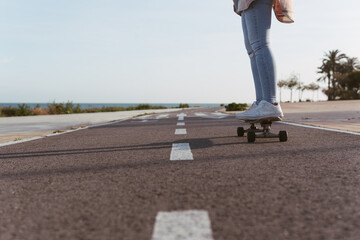 Woman riding her longboard along the promenade on the bike path with the sea in the background. Young girl driving in the right lane of a beach asphalt and the air ahead.