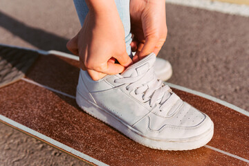 Close-up image of a woman's foot on top of a longboard tying her shoe laces. Perpendicular shot of a woman's shoe ready to go for a spin on the skate.