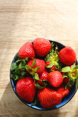 Bowl of fresh strawberries on wooden table, illuminated by sunlight. Flat lay.