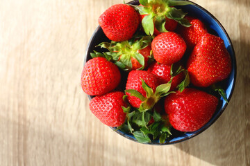 Bowl of fresh strawberries on wooden table, illuminated by sunlight. Flat lay.