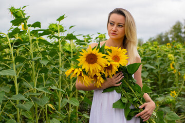 Young beautiful woman with a bouquet of sunflowers in a field of sunflowers