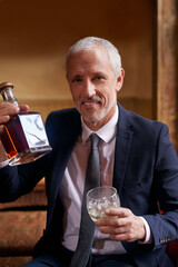 Theres nothing better than a fine whiskey. Portrait of a well-dressed mature man holding a glass and whiskey bottle in a bar after work.