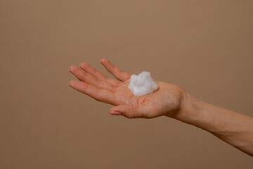 Foam for cleansing the face on a woman's palm. Facial cleansing foam. Foam in a woman's hand. White foam on a beige background. organic cosmetics