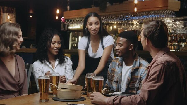Waitress bringing group of friends at restaurant their bill and removing empty plates from table.