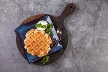 Homemade freshly baked belgian waffles with mint leaves on dark background.