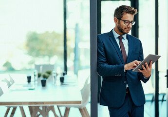 Controlling his business with just a tap. Shot of a young businessman using a digital tablet in an...