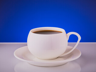 Cup of coffee in a white cup with saucer on a blue background.